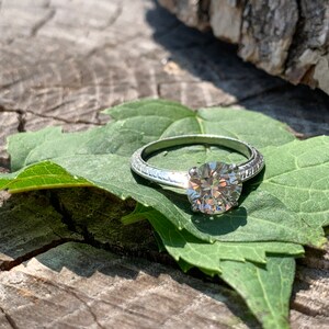 May include: A silver engagement ring with a round diamond set on a green leaf.