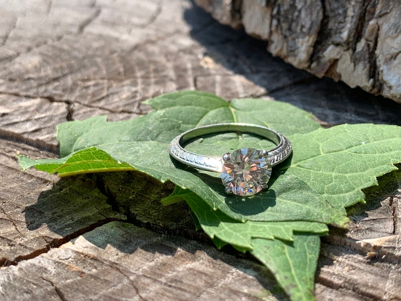 May include: A silver engagement ring with a round diamond set on a green leaf.