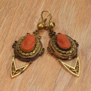 May include: A pair of antique gold earrings with coral cameo insets. The earrings feature a delicate filigree design and a drop-shaped pendant.