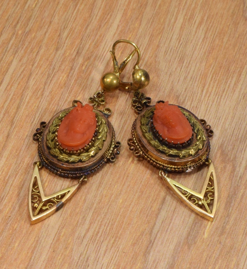 May include: A pair of antique gold earrings with coral cameo insets. The earrings feature a delicate filigree design and a drop-shaped pendant.