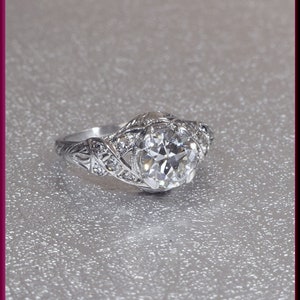 May include: A silver ring with a large, round, clear diamond set in a delicate, intricate design.