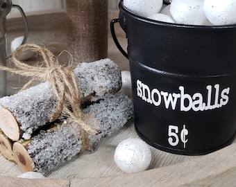May include: A black metal bucket filled with white styrofoam snowballs. The bucket has the words "snowballs 5¢" written on the side.