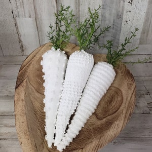 May include: Three white fabric carrots in a wooden bowl. The carrots are made of a soft, textured fabric and have a slightly distressed look.