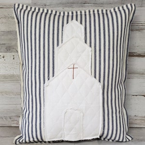 Może przedstawiać: Biała pikowana poduszka z aplikacją w kształcie kościoła na tle niebiesko-białego materiału w paski.