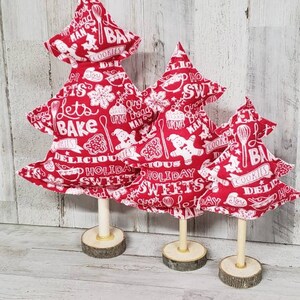 May include: Three red fabric Christmas trees with white text and images of baking-themed designs. The trees are on wooden bases.