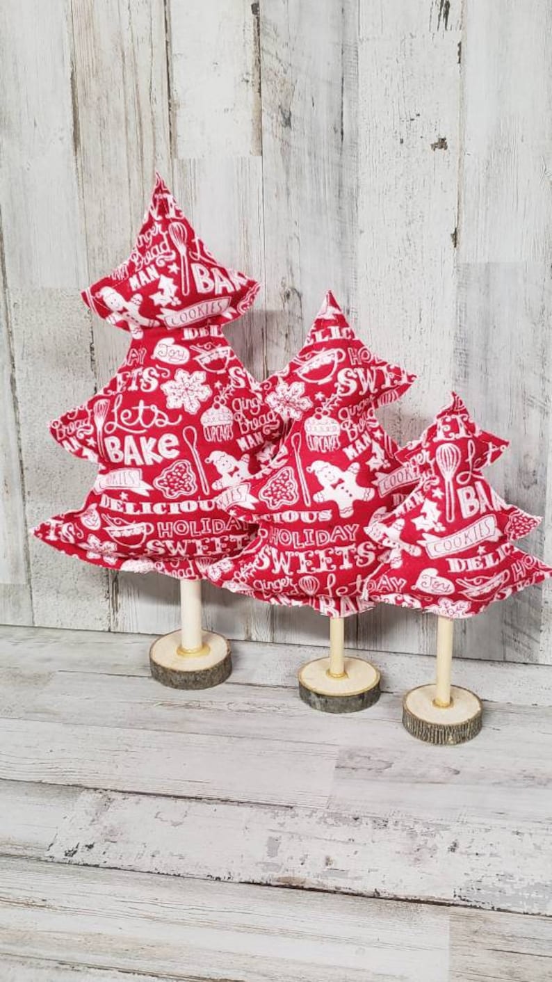 May include: Three red fabric Christmas trees with white text and images of baking-themed designs. The trees are on wooden bases.