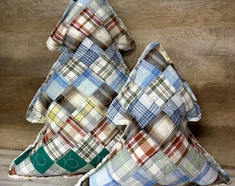 May include: Three tree-shaped decorative pillows. The pillows are made of patchwork fabric in various plaid patterns, including blue, red, green, and yellow. The pillows are arranged on a wooden surface.