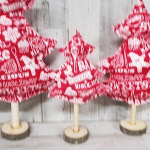 May include: Three red fabric Christmas trees with white lettering and designs. The trees are on wooden bases.