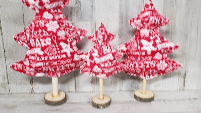 May include: Three red fabric Christmas trees with white lettering and designs. The trees are on wooden bases.