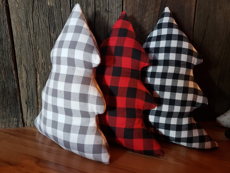 K&ouml;nnte beinhalten: Drei Weihnachtsbaum-f&ouml;rmige Kissen. Eines ist in grau-wei&szlig;em Gingham, eines in rot-schwarzem Buffalo-Karomuster und eines in schwarz-wei&szlig;em Gingham.