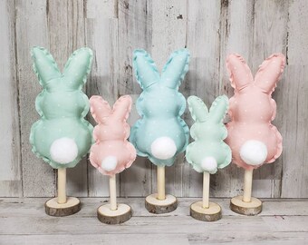 May include: Set of four pastel bunny figurines with white polka dots. The bunnies are made of fabric and have white fluffy tails. They are standing on wooden bases.