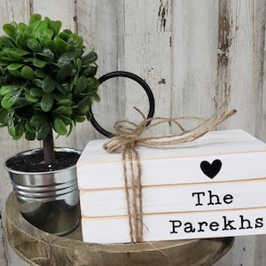 May include: A stack of three white wooden blocks with the words "The Parekhs" and a black heart on the top block. The blocks are tied together with twine and are sitting on a wooden surface.