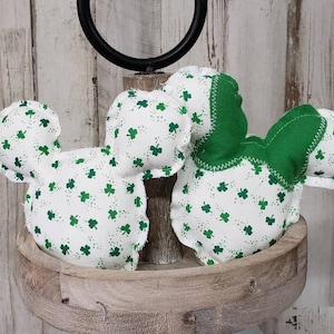 Puede incluir: Dos tréboles de tela blanca con estampado de trébol verde y detalles de tela verde. Los tréboles están sobre una bandeja de madera de dos niveles.