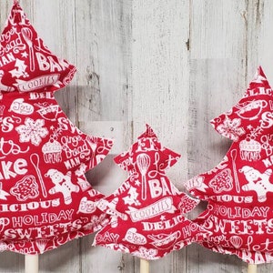 May include: Three red fabric Christmas tree ornaments with white text and designs. The text includes "Let's Bake", "Delicious Holiday Sweets", and "Gingerbread Man".