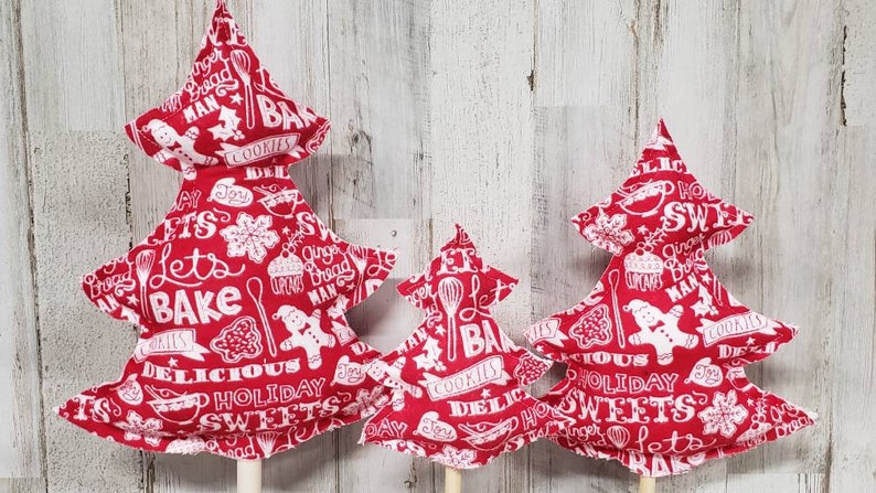 May include: Three red fabric Christmas tree ornaments with white text and designs. The text includes "Let's Bake", "Delicious Holiday Sweets", and "Gingerbread Man".
