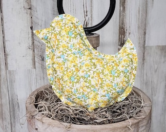 May include: A yellow and blue floral patterned bird-shaped pillow sits in a wooden nest. The pillow is made of fabric and has a soft, cuddly texture.