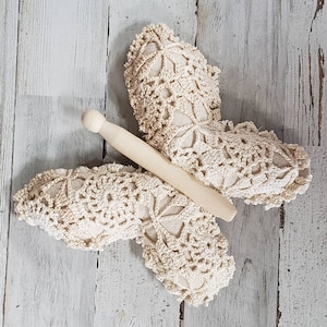 May include: A crocheted butterfly wall decoration with a wooden dowel attached to the centre. The butterfly is cream coloured and has a delicate lace pattern.