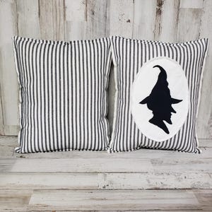 May include: Two black and white striped throw pillows. One pillow has a white circle with a black silhouette of a witch wearing a hat.