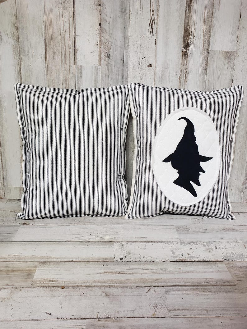 May include: Two black and white striped throw pillows. One pillow has a white circle with a black silhouette of a witch wearing a hat.