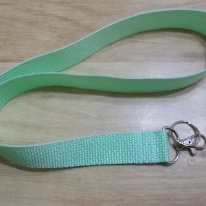 May include: A light green lanyard with a silver key ring. The lanyard is made of a woven fabric.