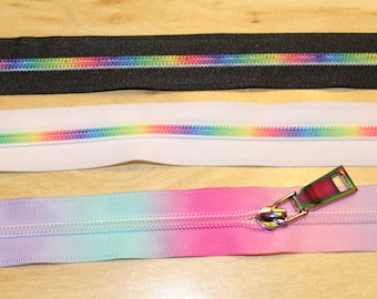 May include: Three zipper tapes with rainbow colored teeth. The top tape is black, the middle tape is white, and the bottom tape is a gradient of pink, purple, and blue.
