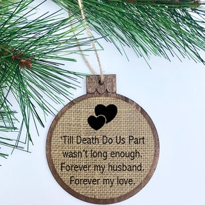 Puede incluir: Un adorno de Navidad de madera con una superficie de arpillera y texto negro que dice: "'Till Death Do Us Part wasn't long enough. Forever my husband. Forever my love." El adorno presenta dos corazones negros.