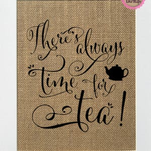 Peut inclure: Impression sur toile de jute encadrée avec l'inscription noire "There's always time for tea!". Une silhouette noire de théière est à côté des mots. Bordure blanche et logo rose en haut à droite.