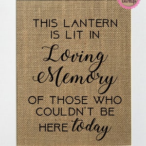 以下が含まれることがあります： 「THIS LANTERN IS LIT IN Loving Memory OF THOSE WHO COULDN'T BE HERE today」と書かれた麻の看板。白い枠で囲まれています。