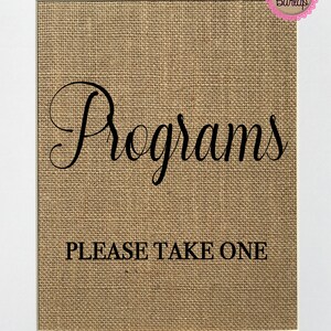 Puede incluir: Un letrero de arpillera con un marco blanco y el texto "Programs" en una fuente cursiva. Debajo del texto está la frase "Please Take One" en una fuente sans-serif.