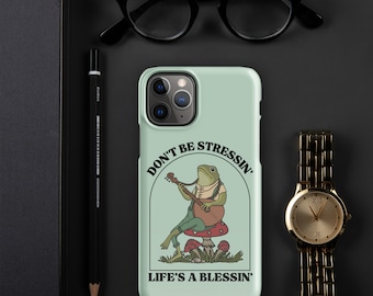 May include: A light green phone case with a cartoon frog playing a banjo. The frog is sitting on a mushroom and there are other mushrooms around it. The text on the case says "Don't be stressin' Life's a blessin'".