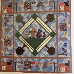 May include: A quilt depicting a family of four figures standing in a field with two trees and a fence. The quilt is made with a variety of fabrics and colors, including blue, green, red, and white. The quilt is titled "Sue and Family" and is hand appliquéd and machine quilted by Sandy Klop, from designs by Janet Ose.