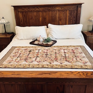May include: A bedroom scene featuring a wooden bed frame and headboard. The bed is made with white linens and a patterned quilt. Two white pillows rest against the headboard. Two nightstands with lamps flank the bed.