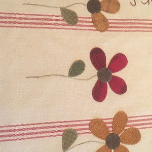 May include: A white kitchen towel with red stripes features three embroidered flowers. The flowers are brown, red, and orange with green leaves. The word "Spring" is embroidered in the top right corner.