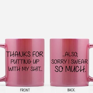 Peut inclure: Une tasse à café en céramique rose avec une poignée noire. Le devant de la tasse est inscrit "THANKS FOR PUTTING UP WITH MY SHIT..." et le dos est inscrit "...ALSO, SORRY I SWEAR SO MUCH."