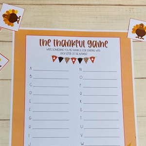 May include: Thanksgiving game sheet with the text "the thankful game" and prompts for each letter of the alphabet. The sheet has an orange border and is decorated with fall leaves. Small turkey illustrations are scattered around the sheet.