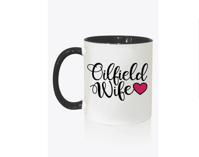 May include: White ceramic mug with a black handle and interior. The mug features the words "Oilfield Wife" in a cursive font, with a pink heart replacing the word "love". The mug is designed for hot or cold beverages.