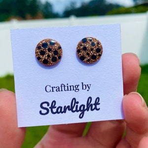 May include: A pair of round stud earrings with a brown and black leopard print design. The earrings are on a white card with the text "Crafting by Starlight".