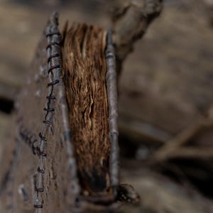 May include: A weathered, leather-bound journal with aged, yellowed pages. The cover is a dark brown with visible stitching along the spine. The book is open, revealing the texture of the paper. The overall aesthetic suggests a vintage or antique item.