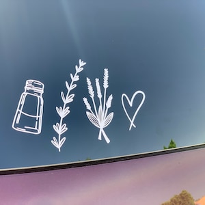 May include: A white vinyl decal featuring a line art illustration of a salt shaker, a single sprig of lavender, a small bouquet of lavender, and a hand-drawn heart shape. The design is applied to a dark, reflective surface, showing clean lines.