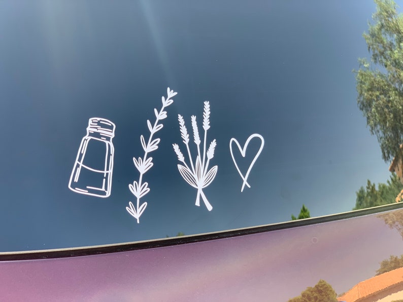 May include: A white vinyl decal featuring a line art illustration of a salt shaker, a single sprig of lavender, a small bouquet of lavender, and a hand-drawn heart shape. The design is applied to a dark, reflective surface, showing clean lines.