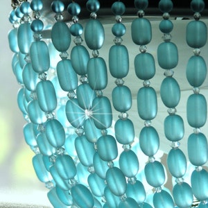 May include: A chandelier made of light blue glass beads. The beads are oval shaped and hang in rows. The chandelier is lit from behind, creating a sparkling effect.