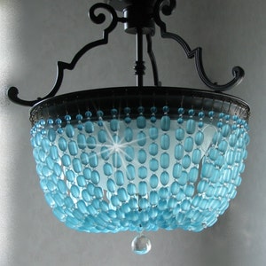 May include: A black metal chandelier with a blue glass bead shade. The beads are arranged in a cascading pattern and the chandelier has a single crystal drop hanging from the bottom.