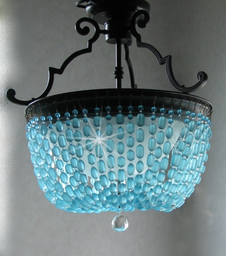 May include: A black metal chandelier with a blue glass bead shade. The beads are arranged in a cascading pattern and the chandelier has a single crystal drop hanging from the bottom.