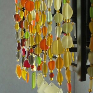 Puede incluir: Una cortina de cuentas hecha de cuentas de vidrio en varios colores, incluyendo naranja, amarillo, verde y blanco. Las cuentas est&aacute;n enhebradas en alambre y cuelgan de un marco de metal negro.