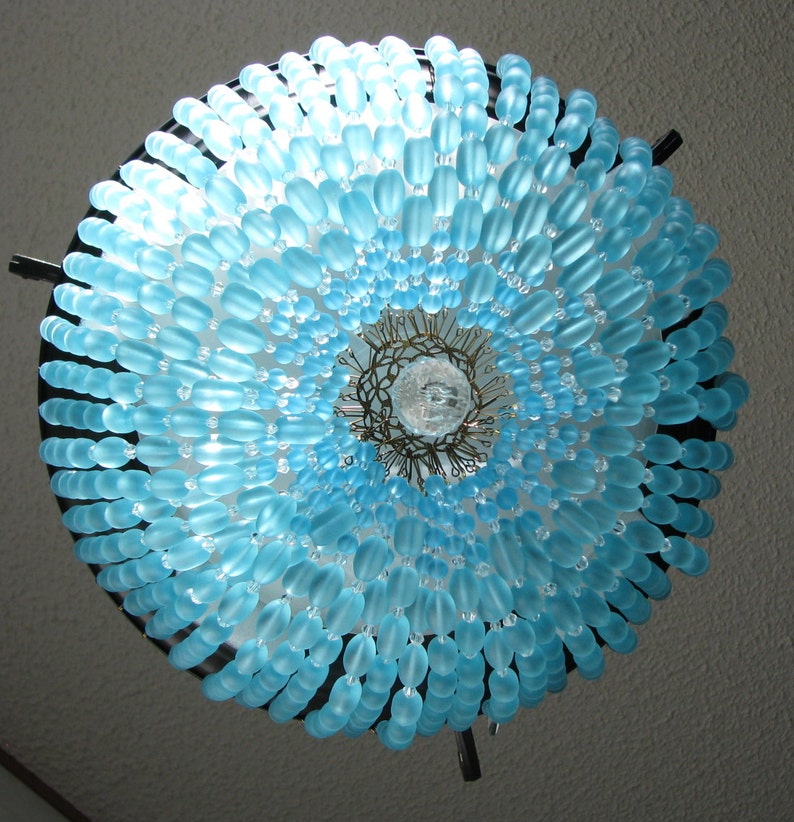 May include: A blue glass bead chandelier with a circular design. The beads are arranged in a spiral pattern, creating a gradient effect from light to dark blue.