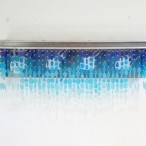 May include: A silver metal light fixture with a row of blue and clear glass beads hanging down. The beads are arranged in a gradient from dark blue to light blue.