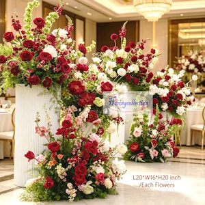 Puede incluir: Arreglos florales con rosas rojas, dalias blancas y vegetación. Las flores están dispuestas sobre pedestales blancos. El texto "Haringcollection" es visible. Dimensiones: L51*A41*H51 cm.