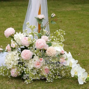 May include: A wedding arch decorated with pink and white flowers, including roses, hydrangeas, and baby's breath. White sheer fabric drapes over the arch.