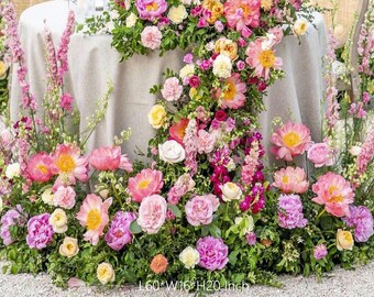 May include: A floral arrangement featuring a variety of pink, yellow, and white flowers, including peonies and roses, with green foliage. The arrangement is approximately 60 inches long, 16 inches wide, and 20 inches high. The flowers are arranged around a table.