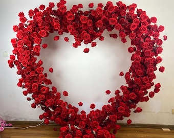 May include: A large heart-shaped floral arrangement made of red silk roses. The roses are arranged in a dense cluster, creating a full and lush look.